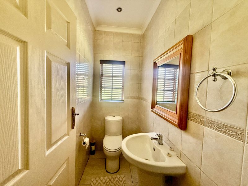 A compact guest bathroom featuring a pedestal basin, toilet, and neutral floor-to-ceiling wall tiles.