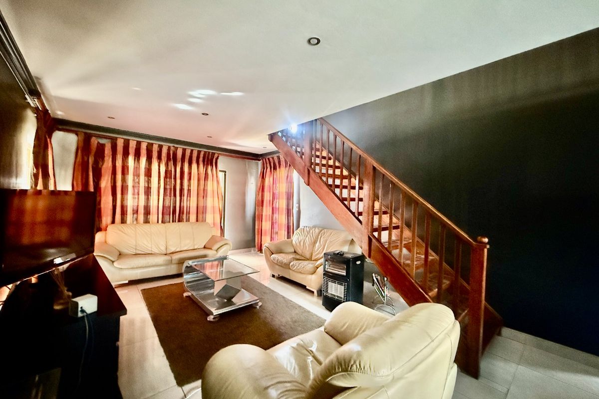 A living room featuring tiled flooring, recessed downlights, and a prominent wooden staircase leading to the upper level.