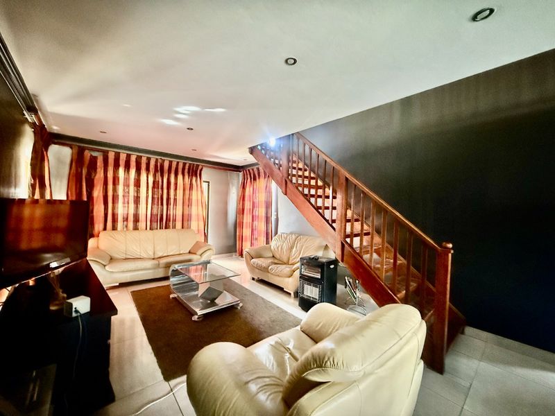 A living room featuring tiled flooring, recessed downlights, and a prominent wooden staircase leading to the upper level.