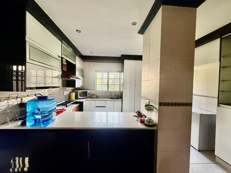 Modern kitchen featuring sleek white cabinetry, stone countertops, a built-in hob with extractor fan, and a tiled backsplash, offering a clean and functional workspace.