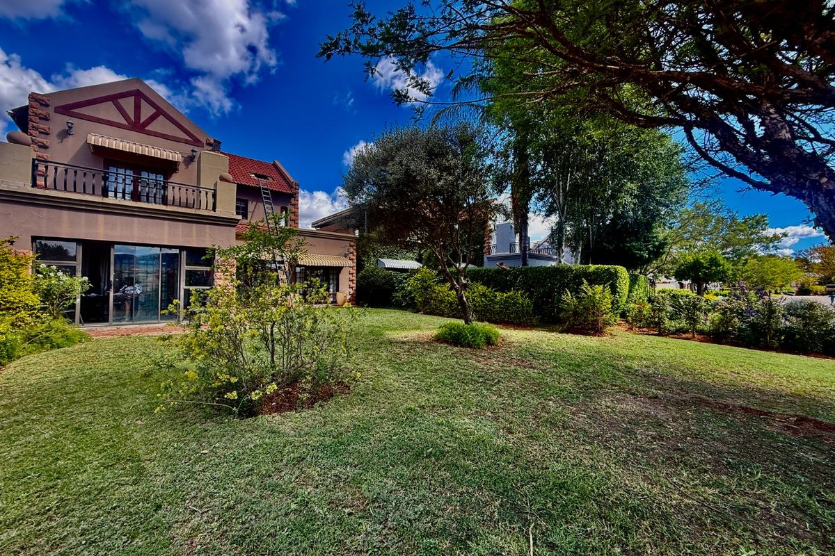 A view of the rear elevation of the house featuring a landscaped garden, lawn, and a balcony accessible via sliding glass doors.