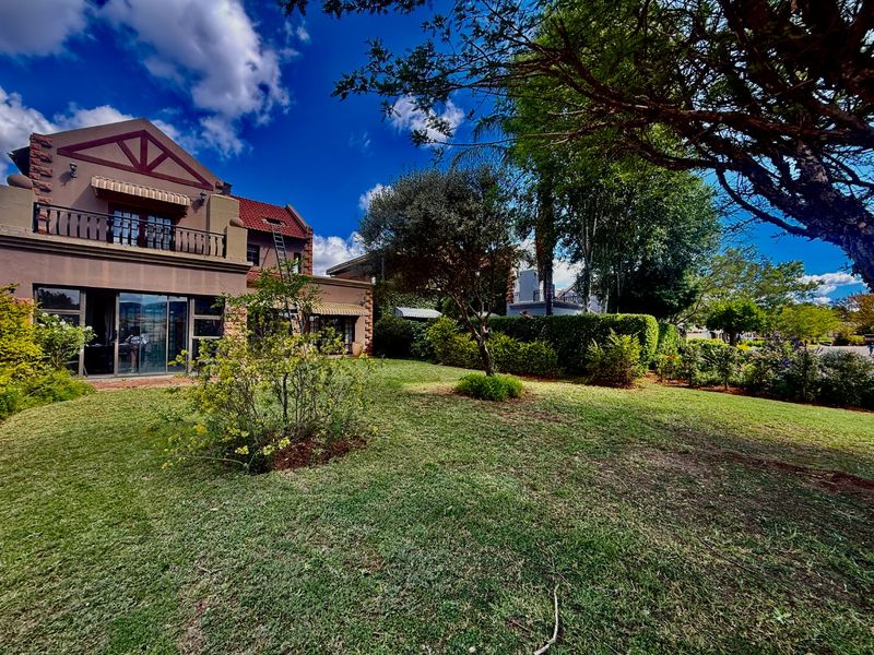 A view of the rear elevation of the house featuring a landscaped garden, lawn, and a balcony accessible via sliding glass doors.