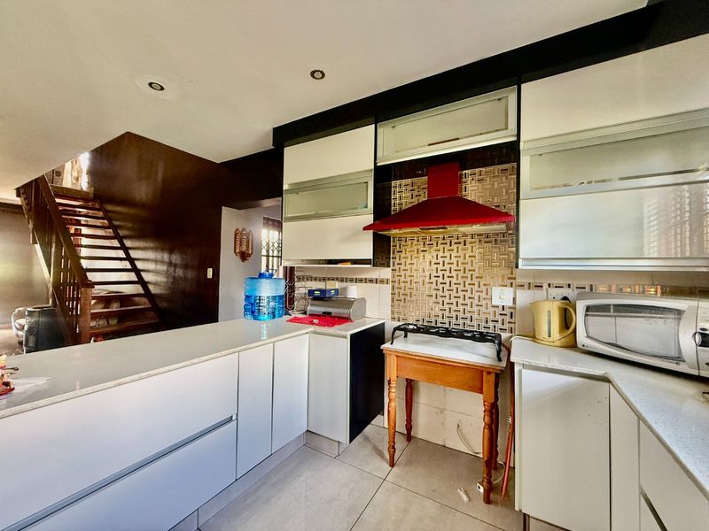 Kitchen featuring modern cabinetry, stone countertops, and a mosaic tile backsplash, with an adjacent staircase leading to the upper level.