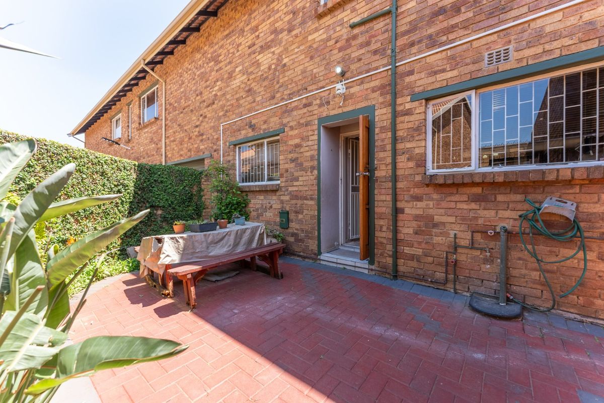 Rear exterior view of the townhouse featuring a paved patio area, brick facade, and security-fitted windows.
