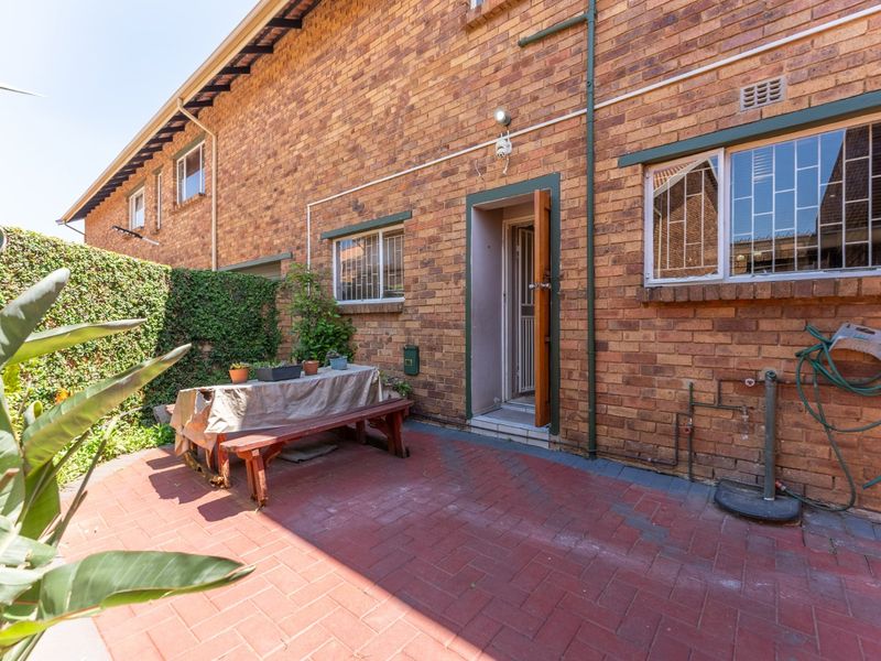 Rear exterior view of the townhouse featuring a paved patio area, brick facade, and security-fitted windows.