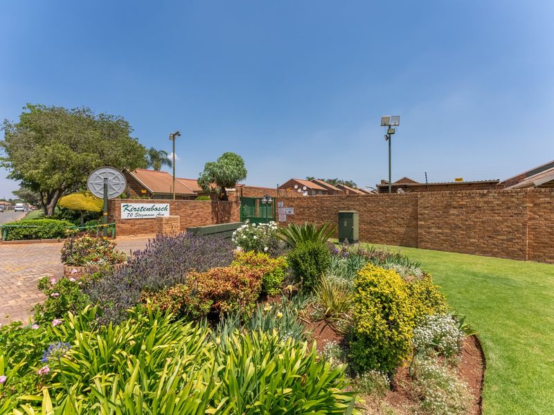 Front entrance view of Kirstenbosch townhouse complex featuring a well-maintained brick boundary wall, landscaped garden, and secure gated access.
