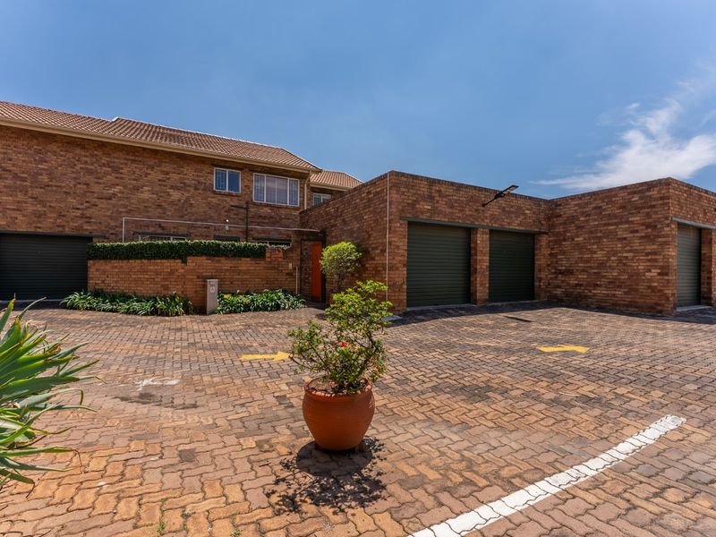 Front exterior view of a brick townhouse complex featuring multiple garage doors and a paved driveway area.