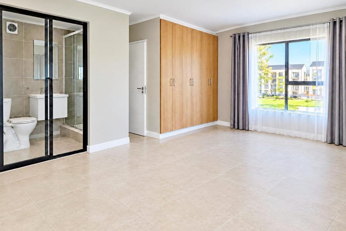 Spacious bedroom featuring neutral tiled flooring, ample built-in cupboard space, and a modern en-suite bathroom with a glass shower enclosure.