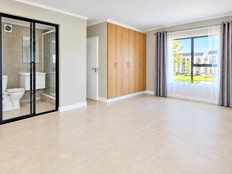 Spacious bedroom featuring neutral tiled flooring, ample built-in cupboard space, and a modern en-suite bathroom with a glass shower enclosure.
