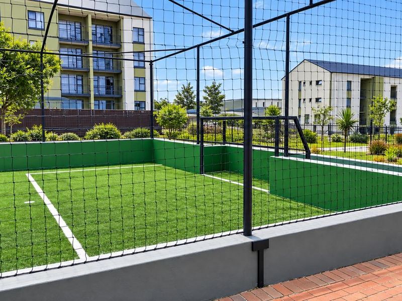 A well-maintained outdoor sports facility featuring an artificial turf court enclosed by perimeter fencing and retaining walls within an apartment complex.