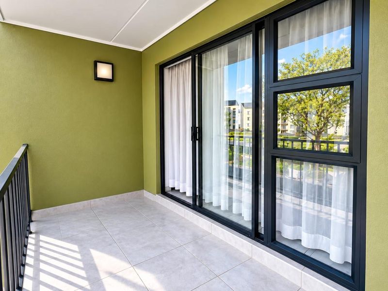 A clean, well-maintained balcony featuring tiled flooring, a black metal balustrade, and modern sliding glass doors with views of the surrounding complex.