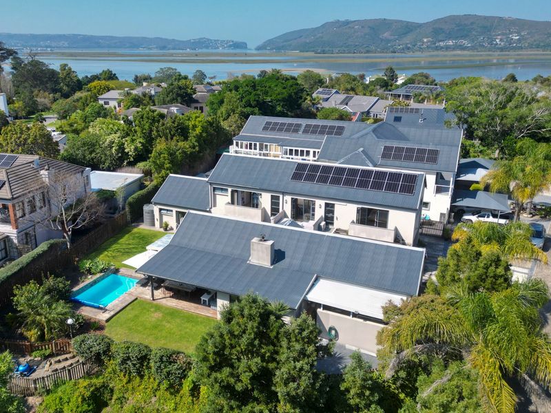 Aerial view of a residential property featuring a metal roof with solar panels, a swimming pool, and a landscaped garden overlooking the estuary.