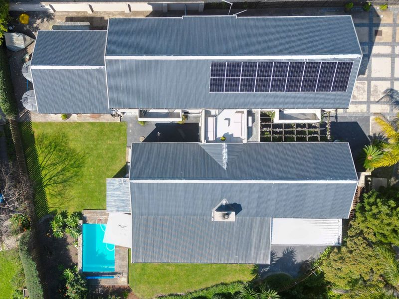 Aerial view of the property showcasing the corrugated metal roof with solar panels, swimming pool, landscaped garden, and paved driveway areas.