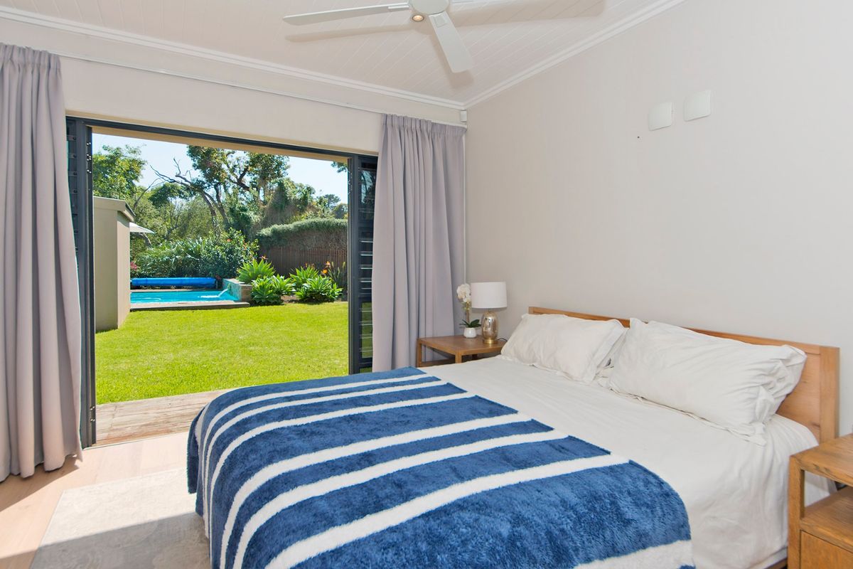 A bright bedroom featuring sliding glass doors that open onto a private timber deck, garden, and swimming pool area.