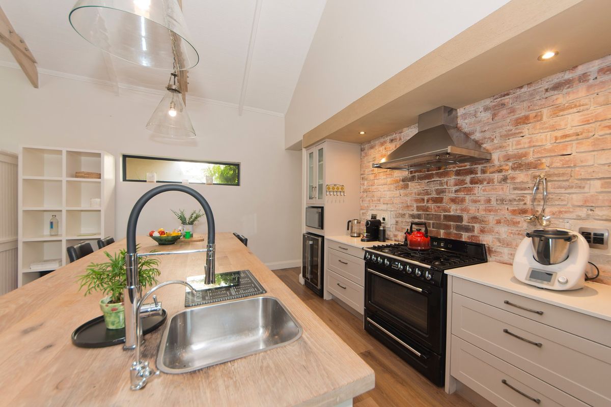 Modern kitchen featuring an exposed brick feature wall, gas range cooker, large island with integrated sink, and vaulted ceilings with pendant lighting.