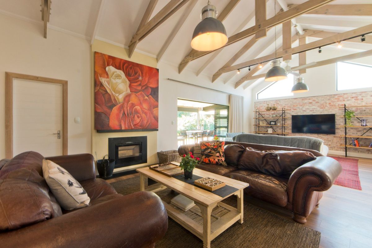Spacious living room featuring a vaulted ceiling with exposed timber trusses, a built-in fireplace, and an exposed brick feature wall with seamless outdoor access.