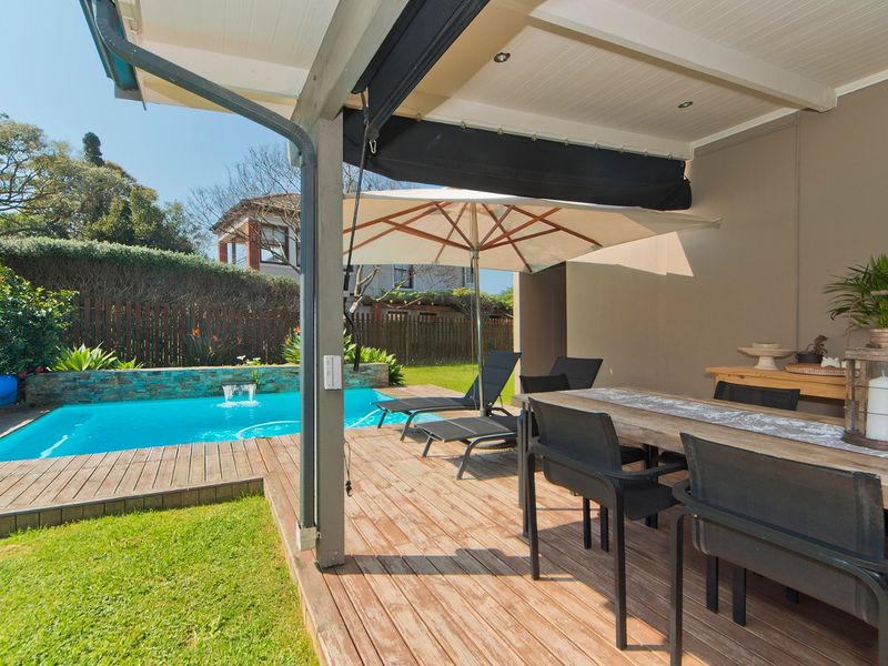 A covered timber deck patio overlooking a swimming pool with a stone-clad water feature and landscaped garden.