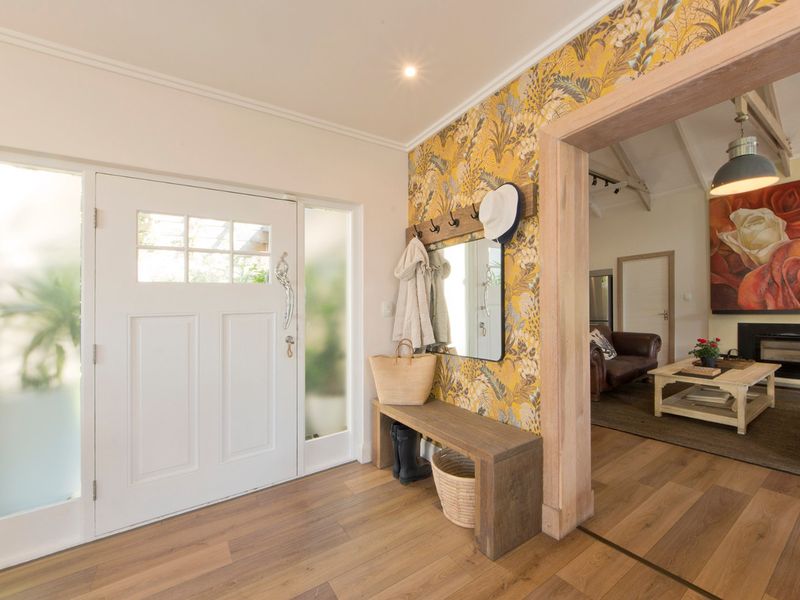 Welcoming entrance hall featuring timber flooring, a solid front door with frosted glass sidelights, and a decorative feature wall leading into the living area.