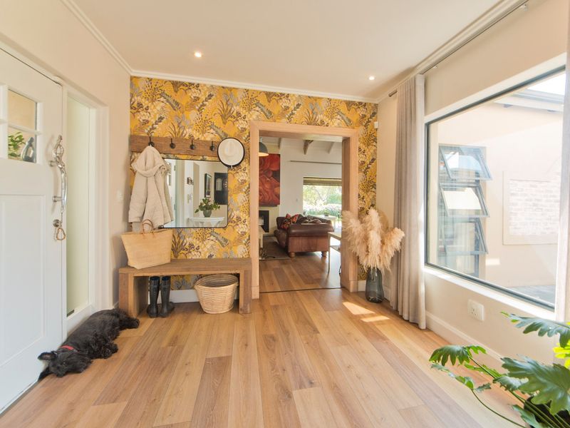 Bright and welcoming entrance hall featuring warm timber flooring, a large picture window, and stylish feature wallpaper leading into the main living area.