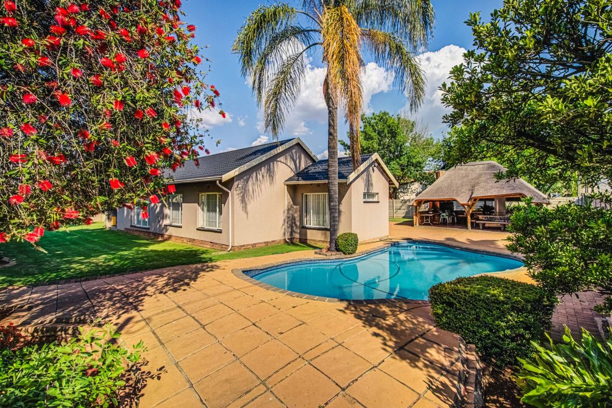 Rear view of the property featuring a well-maintained swimming pool, paved patio area, and a traditional thatched lapa set within a landscaped garden.
