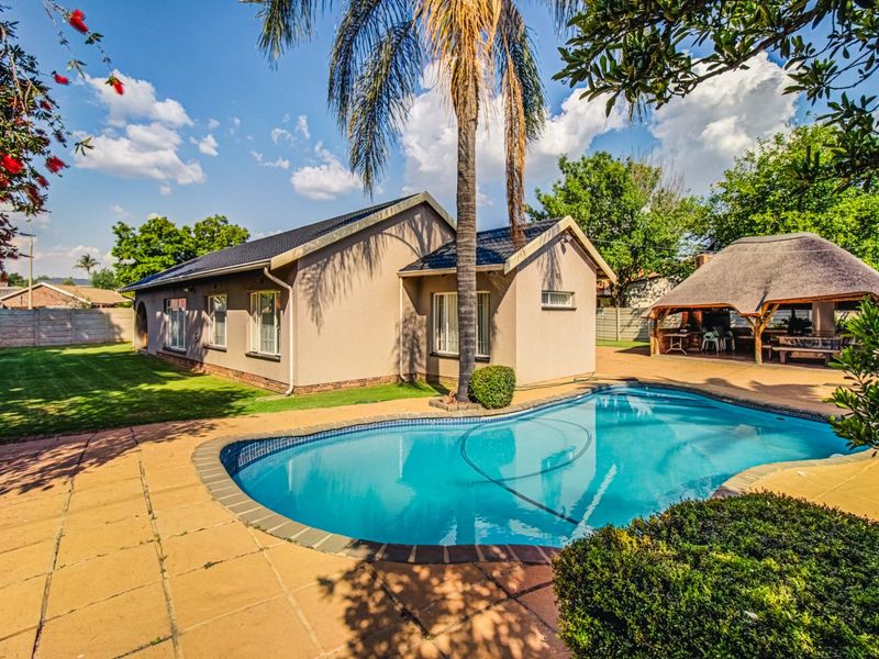 Rear exterior view featuring a swimming pool, paved patio area, and a traditional thatched lapa, set within a well-maintained garden.
