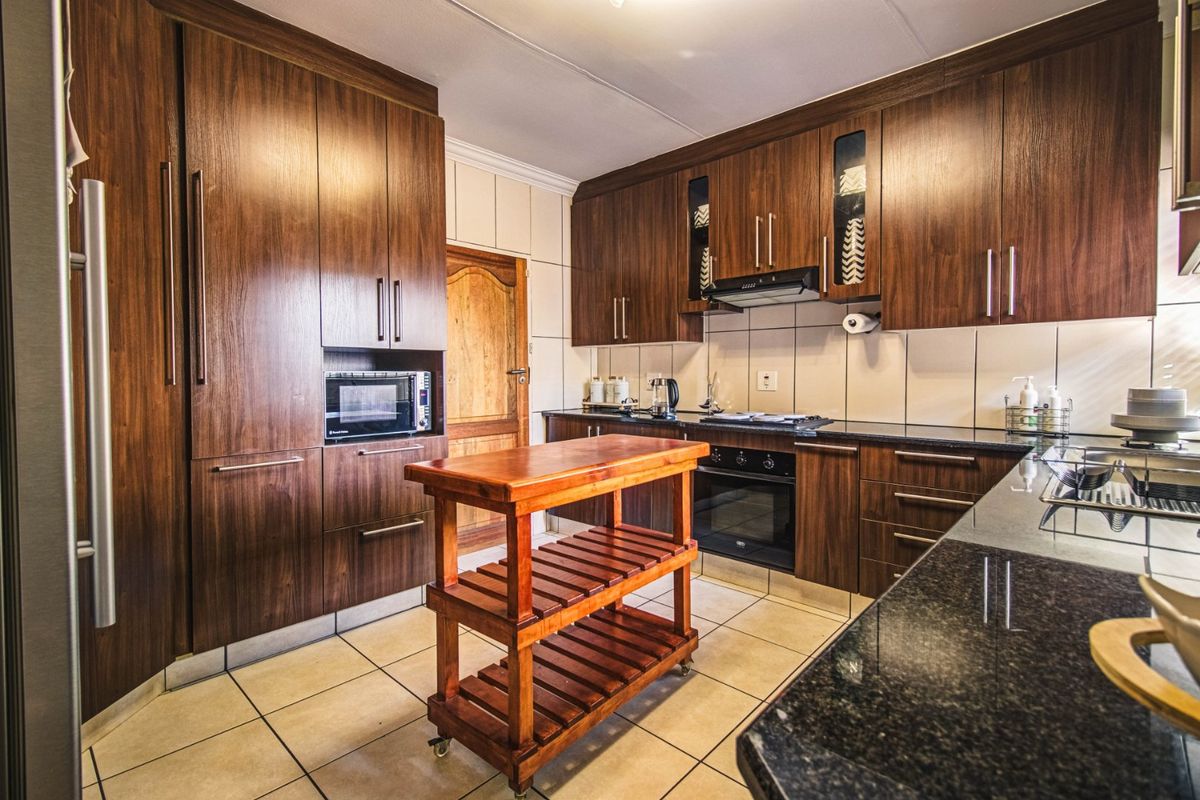 A well-maintained kitchen featuring dark wood cabinetry, granite countertops, built-in oven, hob, and extractor fan with tiled flooring and backsplash.