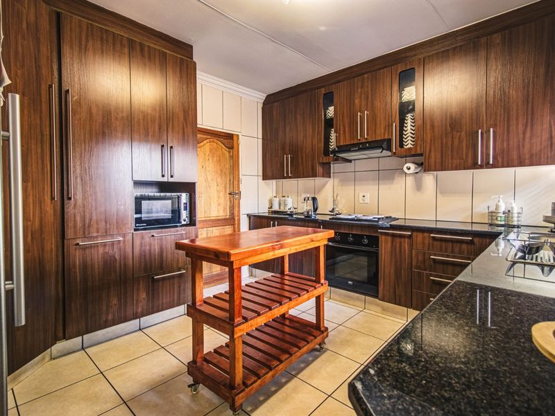 A well-maintained kitchen featuring dark wood cabinetry, granite countertops, built-in oven, hob, and extractor fan with tiled flooring and backsplash.