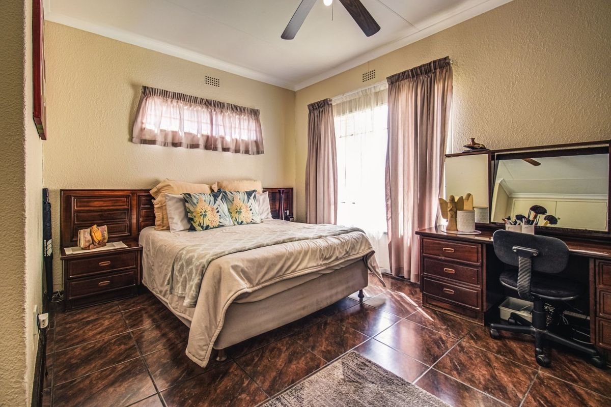 A well-lit bedroom featuring tiled flooring, a ceiling fan, and built-in wooden cabinetry including a headboard and vanity unit.