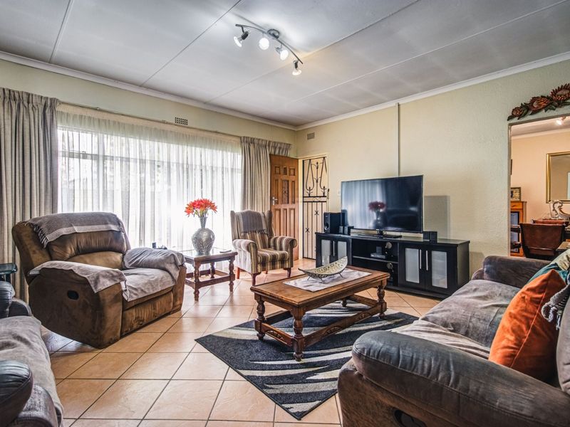 A spacious living room featuring tiled flooring, a large window providing natural light, and a ceiling-mounted spotlight fixture.
