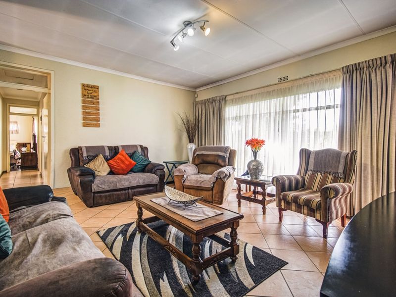 A spacious living room featuring tiled flooring, a ceiling-mounted spotlight fixture, and large windows that provide ample natural light.