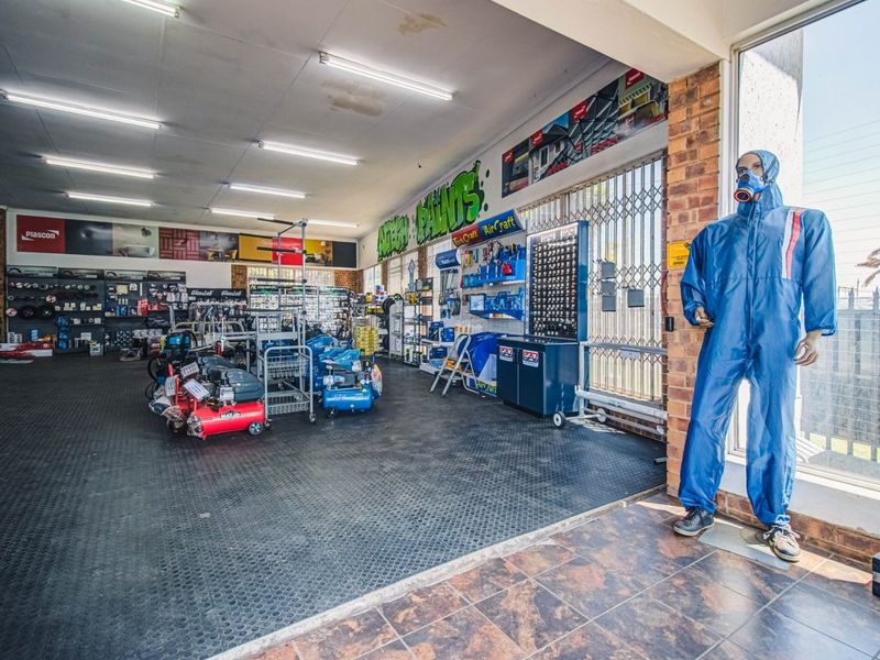 Spacious commercial retail area featuring durable rubber and tiled flooring, large display windows, security gates, and functional overhead fluorescent lighting.