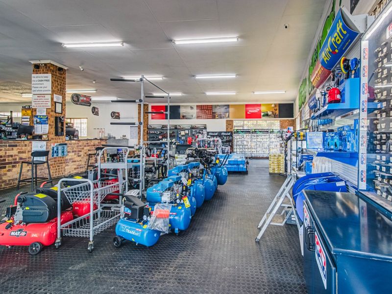 A well-lit commercial retail space featuring durable rubber flooring, exposed brick accents, and a functional service counter, currently utilized for hardware and equipment sales.