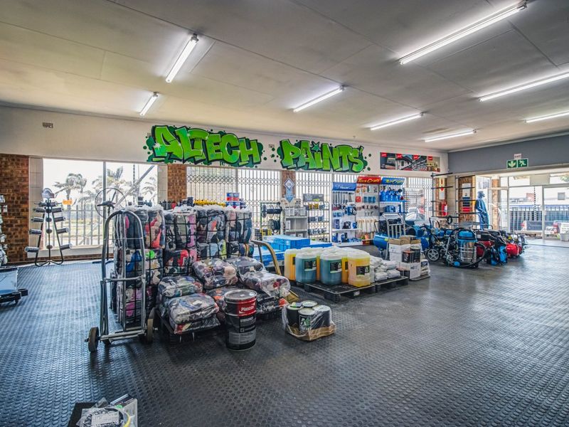Spacious commercial retail or utility area featuring durable rubber flooring, bright fluorescent lighting, and large windows with security gates.