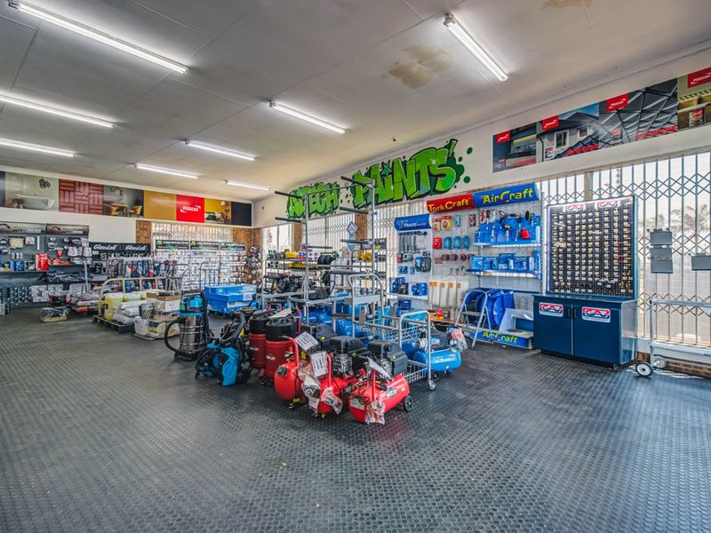 A commercial retail space featuring durable rubber flooring, fluorescent lighting, and built-in display shelving for hardware and paint products.