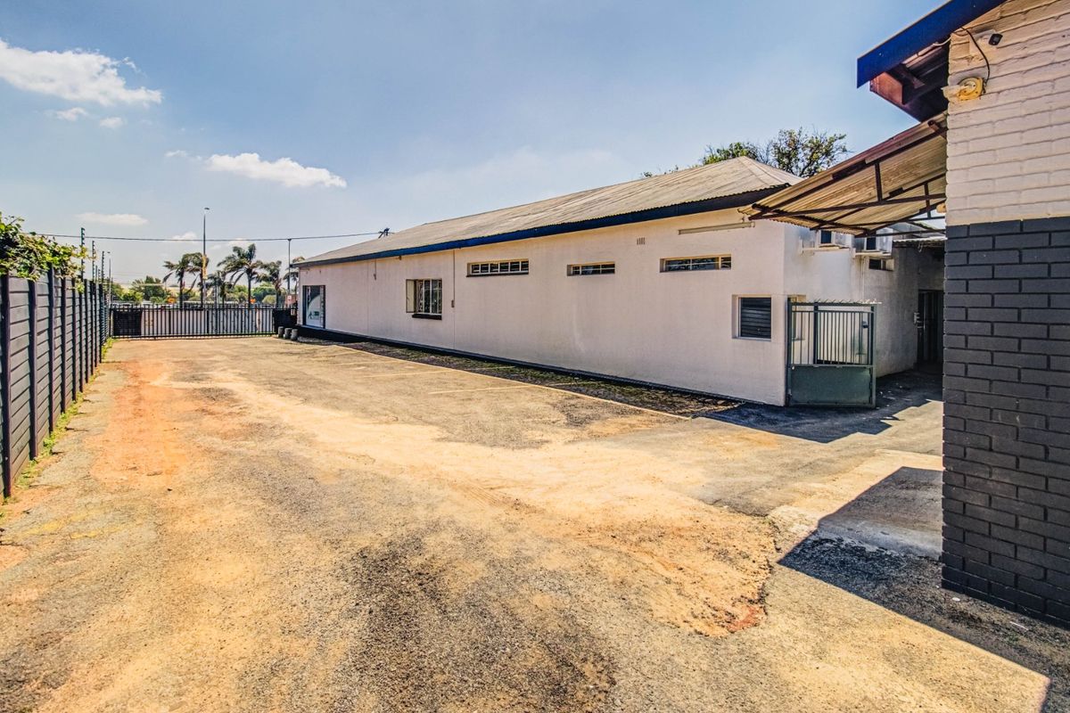 Rear exterior view of the commercial property featuring a large asphalt parking area, security fencing, and a painted brick building facade.