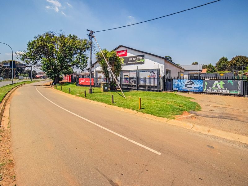 Street-level view of a commercial property featuring secure perimeter fencing, paved access, and prominent signage along the roadside.