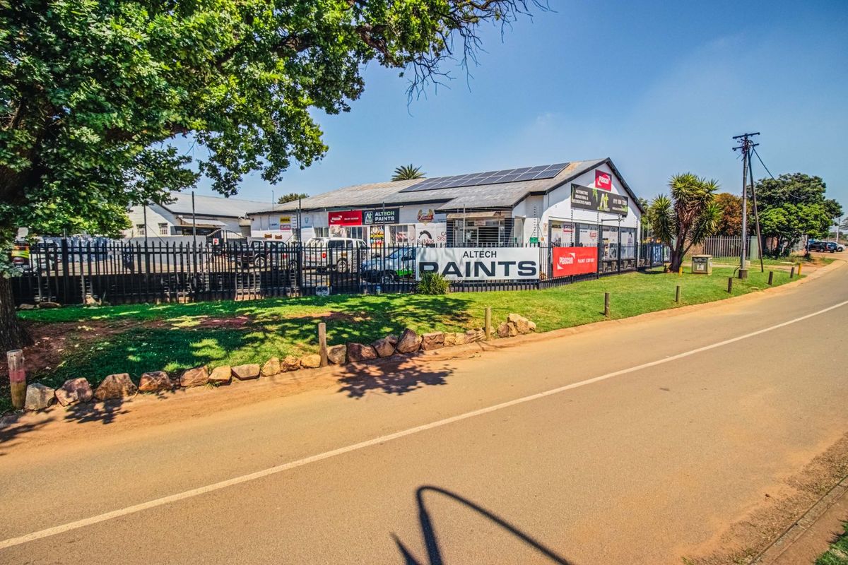 Commercial property frontage featuring solar panels, secure perimeter fencing, and prominent signage along a paved road.