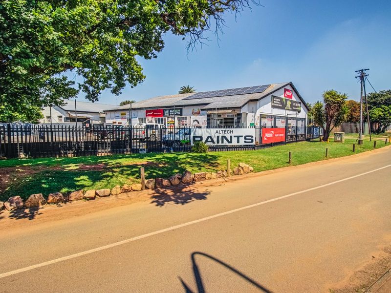 Commercial property frontage featuring solar panels, secure perimeter fencing, and prominent signage along a paved road.