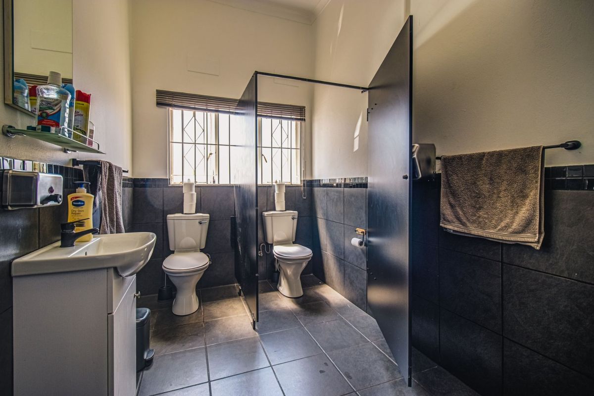 Commercial bathroom facility featuring dual toilets with privacy partitions, tiled finishes, and a wall-mounted vanity basin.