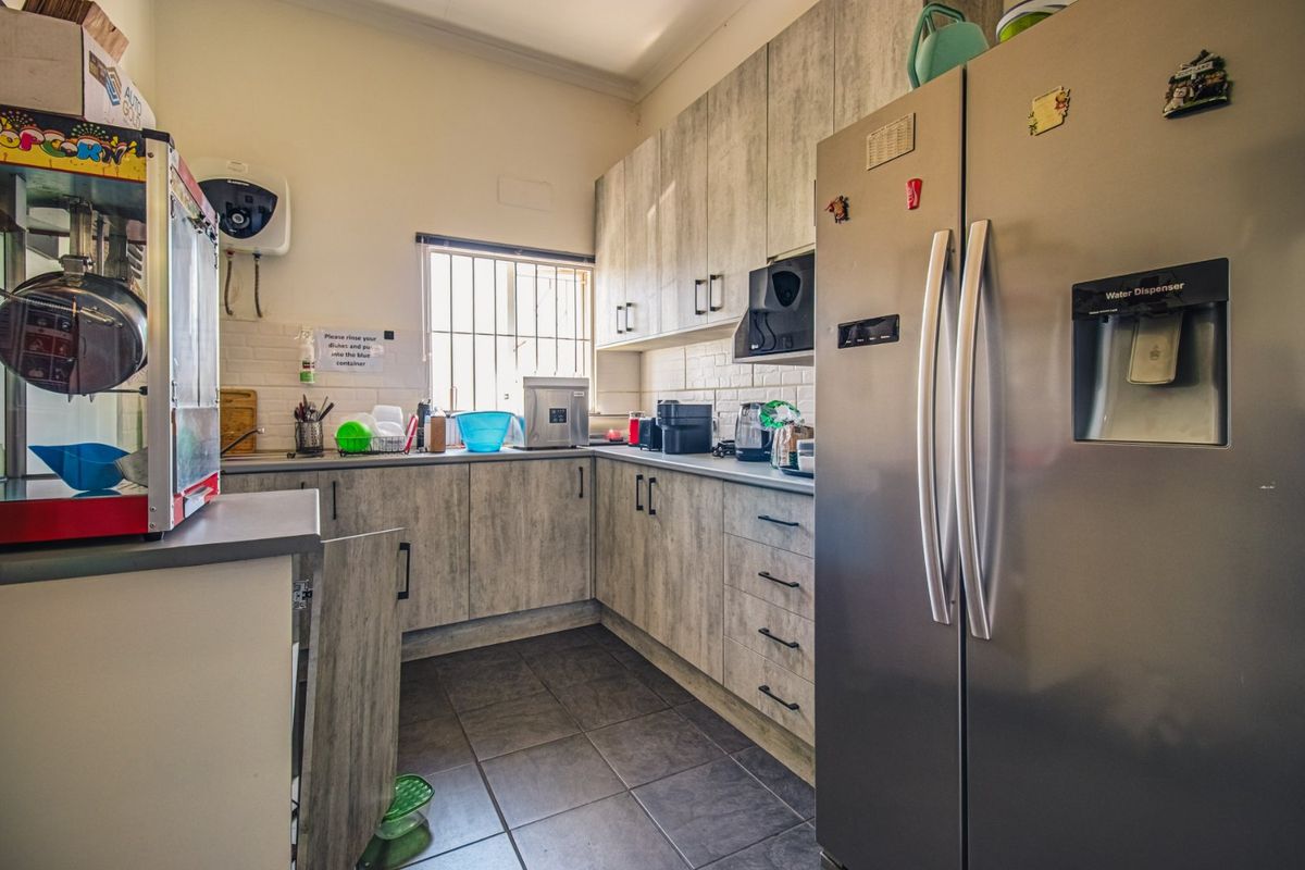 A functional kitchen featuring wood-look cabinetry, tiled flooring, and a tiled backsplash, equipped with essential built-in storage and a wall-mounted water heater.
