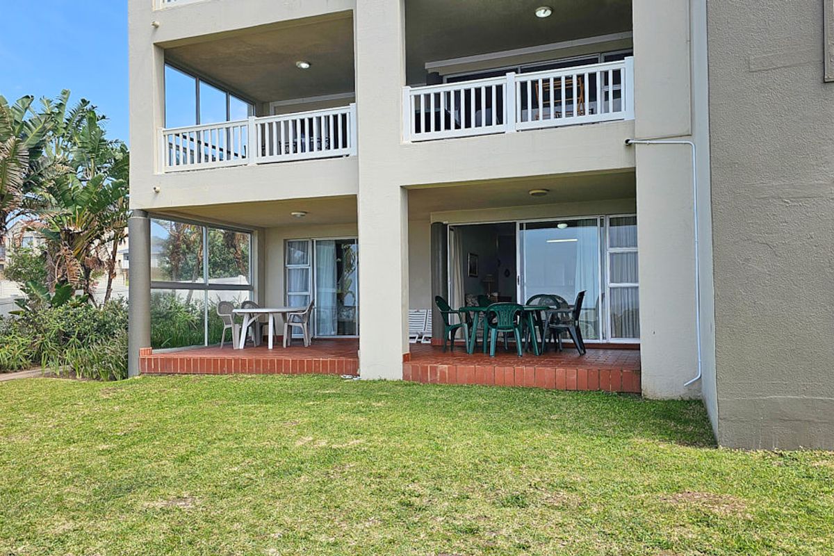 Rear view of the apartment building featuring covered ground-floor patios with brick flooring, white balustrades, and sliding glass door access to the interior.