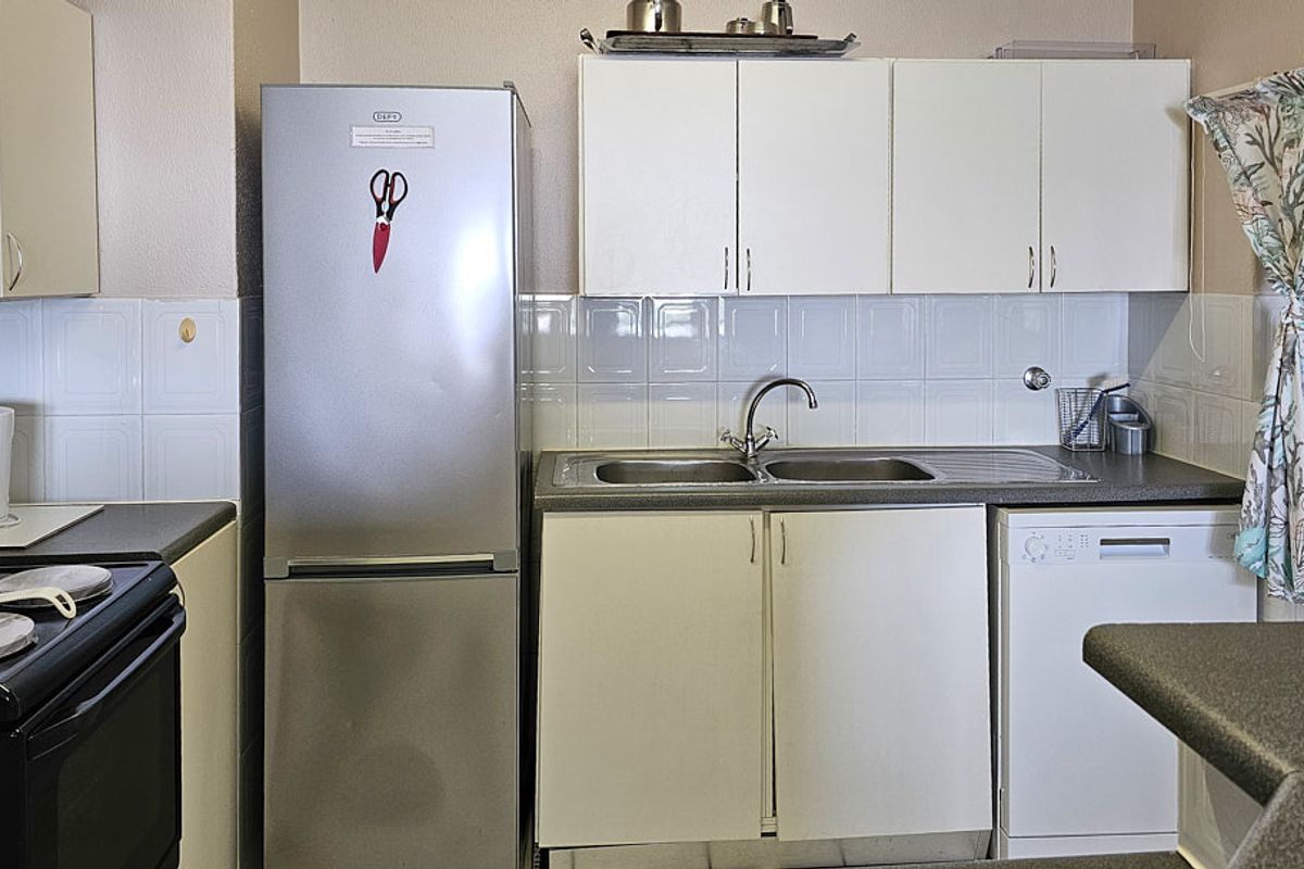 A functional kitchen featuring white cabinetry, a double bowl sink, tiled backsplash, and space for a freestanding stove and dishwasher.