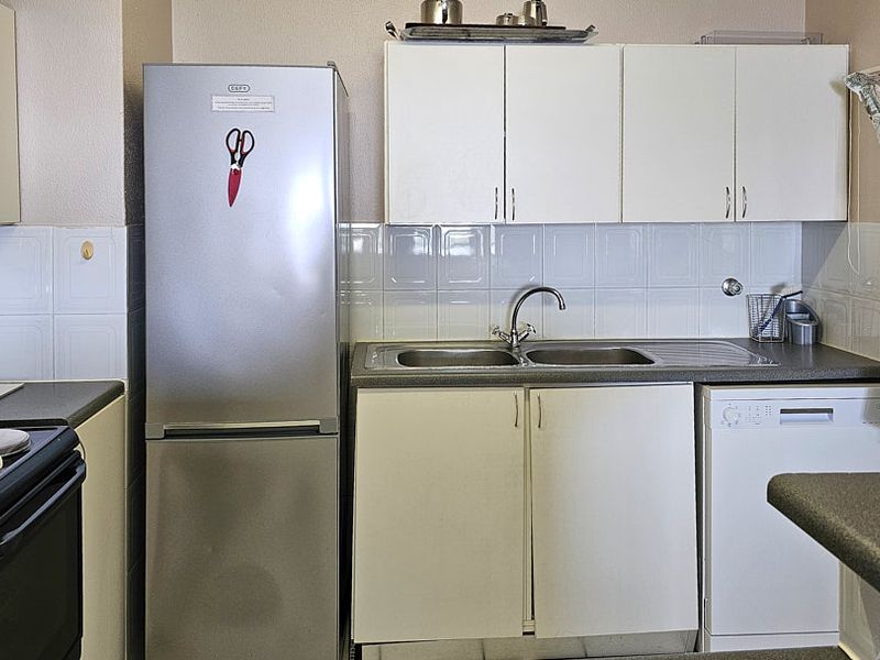 A functional kitchen featuring white cabinetry, a double bowl sink, tiled backsplash, and space for a freestanding stove and dishwasher.
