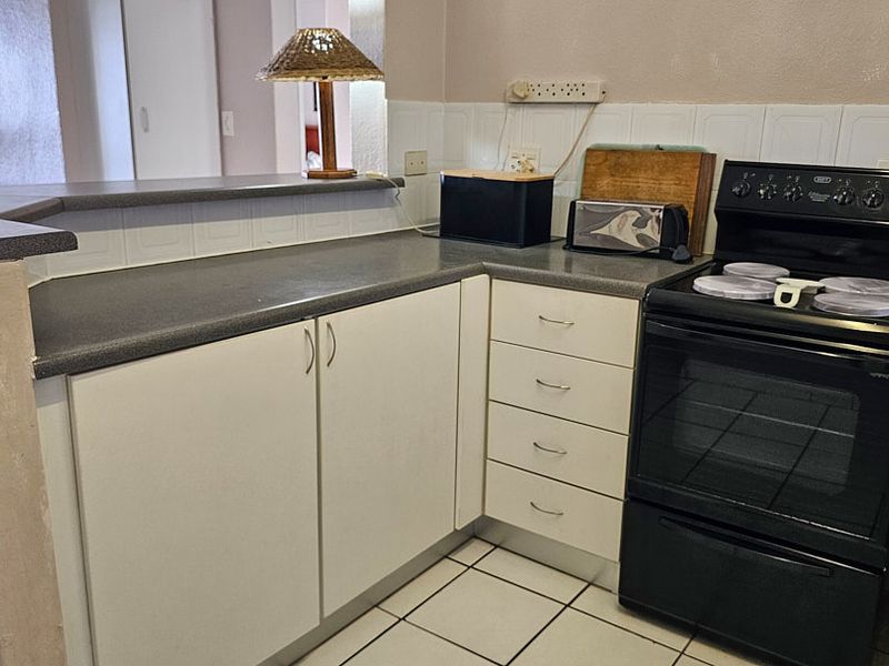 A functional kitchen featuring white cabinetry, laminate countertops, a tiled backsplash, and a freestanding stove, with an integrated breakfast bar overlooking the living area.