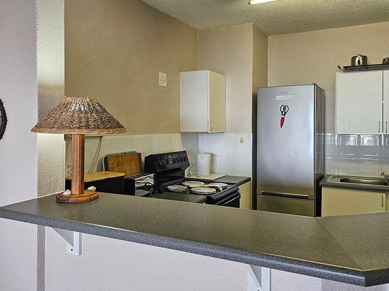 A functional kitchen featuring a breakfast bar, tiled backsplash, stainless steel sink, and built-in cabinetry, offering a practical layout for daily meal preparation.