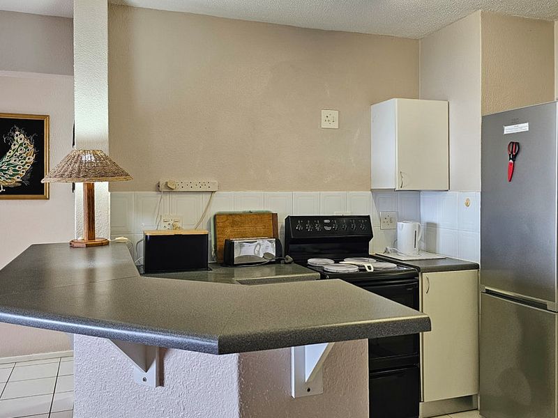 Compact kitchen featuring a breakfast bar, tiled backsplash, and functional cabinetry, offering a practical layout for daily meal preparation.