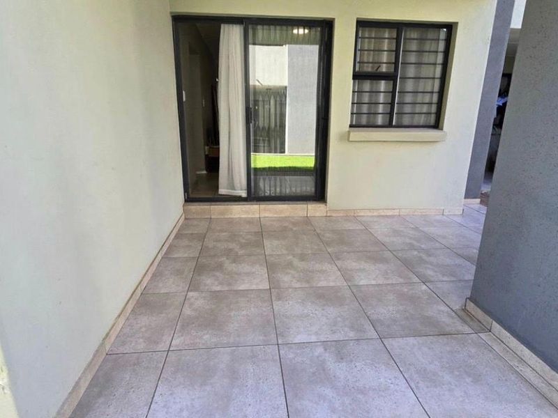 A clean, covered patio area featuring neutral floor tiles, a sliding glass door entrance, and a window with security bars.