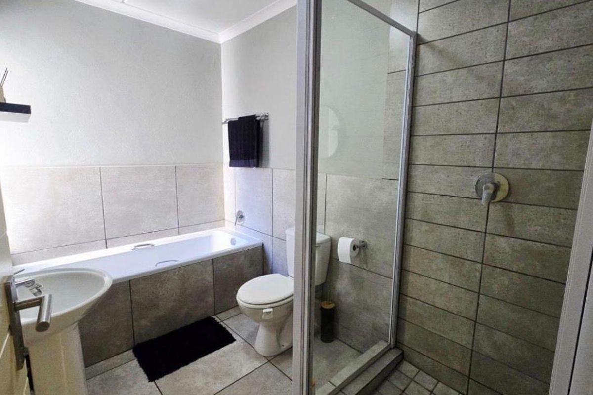 A modern bathroom featuring a pedestal basin, built-in bathtub, and a separate glass-enclosed shower with neutral tiled finishes.