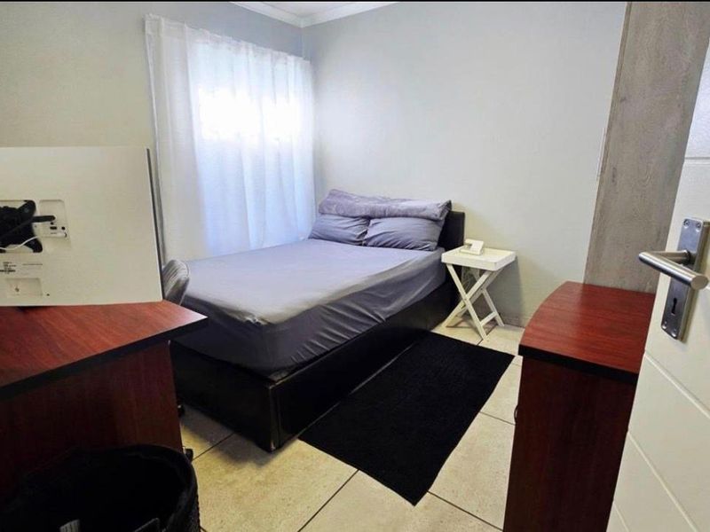 A compact bedroom featuring tiled flooring, a window with curtains, and a standard internal door.