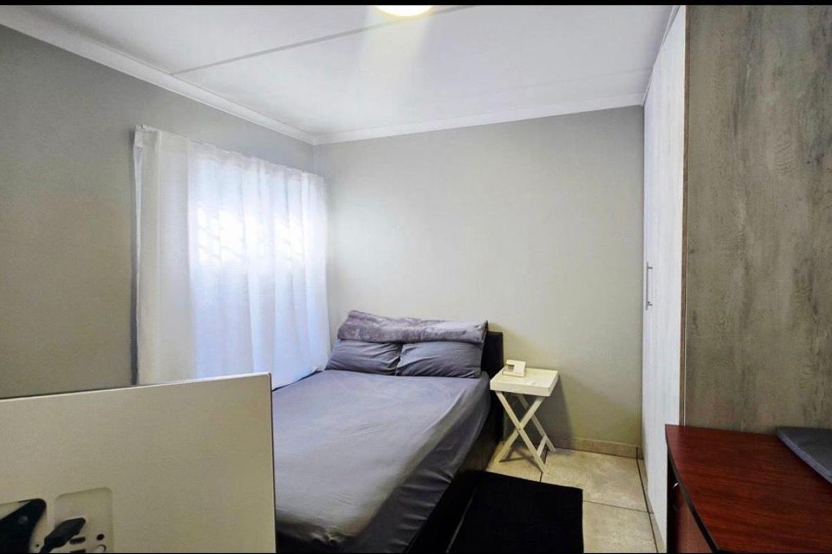 A compact bedroom featuring neutral wall tones, tiled flooring, and a built-in wardrobe, offering a functional and clean living space.